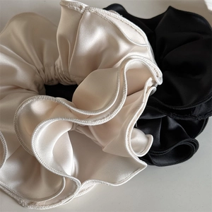 Gros plan de chouchous en satin de qualité en crème et noir avec bords ondulés à volants