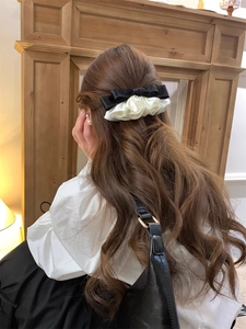 Detail view of a black velvet and white satin ruffle hair clip on brown wavy hair
