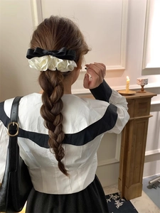 Detail of elegant black and white ruffled satin bow hair clip worn in a French retro style