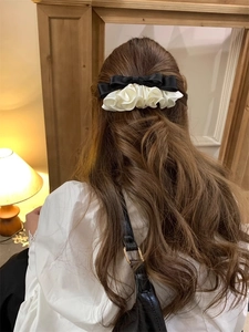 Detail of elegant black satin bow and beige ruffled lace hairpin on long curly hair