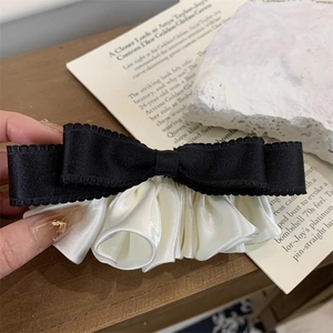 Detail of elegant black ribbon and white satin pleated bow hair clip held by hand
