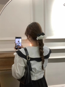 Detail of a white pleated satin scrunchie with a black bow worn on a model's hair