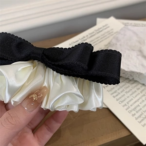 Macro shot of black ribbon bow and white satin pleated hair clip with French style texture