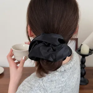 Grand chouchou élégant en satin noir présenté dans une coiffure chic pour femme
