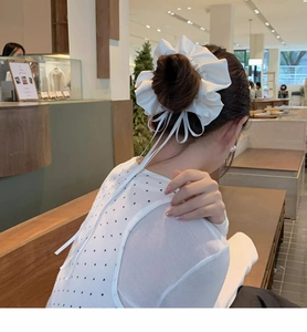 Detailed view of white oversized satin scrunchie with long ribbon bow on high bun