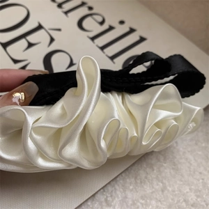 Detailed macro view of the ruffled black and cream satin fabric texture on a hair scrunchie