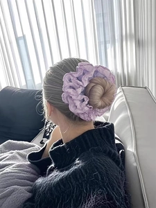 Detail of purple pleated scrunchie with wavy edges worn on a low bun hairstyle
