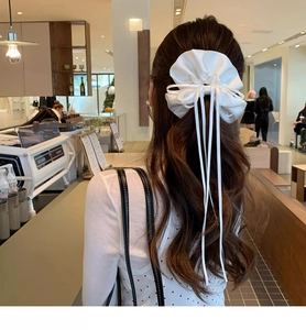 White satin bow hair scrunchie with long ribbons worn on a ponytail for a sweet look