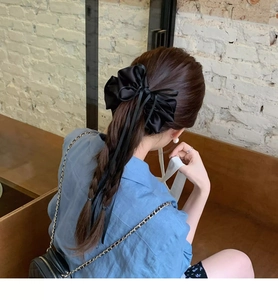 Detail of elegant black satin bow hair tie with long ribbons on a braided hairstyle