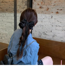 Detail of elegant black satin bow hair scrunchie with ribbons on a braided ponytail