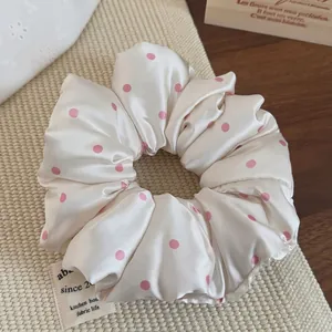 Close-up of cream satin scrunchie with pink polka dots and fabric life label