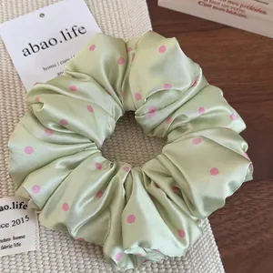 Close-up of light green satin scrunchie with pink polka dots on a wooden table