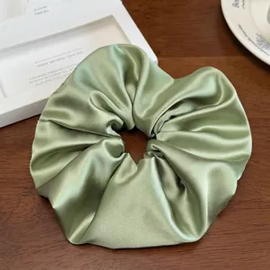 Détail d'un chouchou géant en satin vert sauge posé sur une table en bois foncé