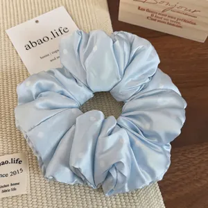 Detail shot of a soft light blue polka dot hair scrunchie with silky pleated fabric texture