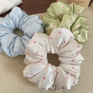 Close-up of soft satin polka dot hair scrunchies in pastel blue, green, and cream colors