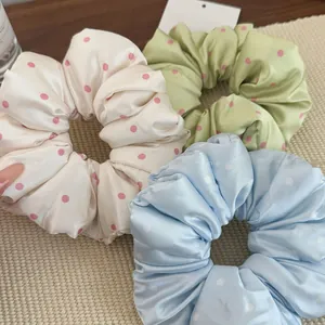 Close-up of three satin pillow scrunchies in cream green and blue with polka dot patterns