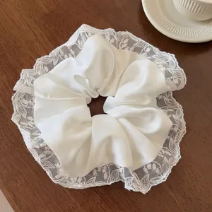 Detailed close-up of white silk scrunchie with embroidered lace edge and small woven tag