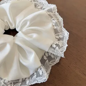Elegant white silk scrunchie with lace trim edges displayed on a brown wooden table