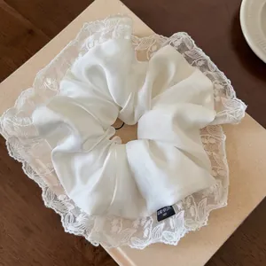 Elegant white satin scrunchie with lace embroidery trim on a premium wooden display