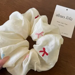 Cremefarbenes Seiden-Scrunchie mit bunten Schmetterlingsstickereien auf dunklem Holz