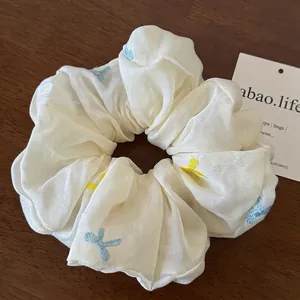 Eleganter cremefarbener Seiden-Scrunchie mit bunten Stickereien auf einer Holzfläche