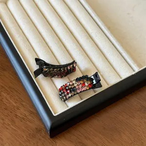 Detail shot of two mini duckbill hair clips with colorful rhinestones on velvet tray