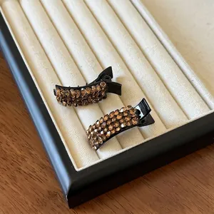 Detail view of two black duckbill hair clips with amber rhinestones on a jewelry tray