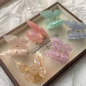 Iridescent 3D butterfly hair claw clips in six pastel colors on a wooden tray
