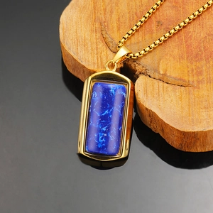 Detailopname van gouden rechthoekige turquoise hanger aan ketting op een houten blok