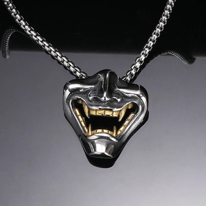 Detail of silver Hannya mask pendant with golden tusks on black reflective surface