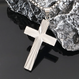 Vue détaillée du pendentif croix en acier argenté avec texture radiale sur chaîne