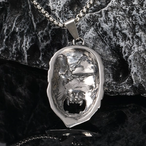 Macro shot of silver stainless steel gothic beast pendant on a box chain over dark rocks