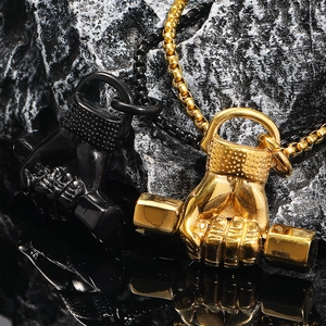 Détail des pendentifs haltère et poing en or et noir sur fond de roche noire brute
