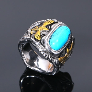 Detalle macro de anillo para hombre en acero de titanio con turquesa y águilas doradas