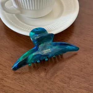 Detailed view of handmade acetate hair claw clip with blue marble pattern on wooden table