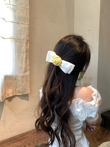 Dettaglio di elegante fiocco in raso bianco con una rosa in tessuto giallo e luce soffusa