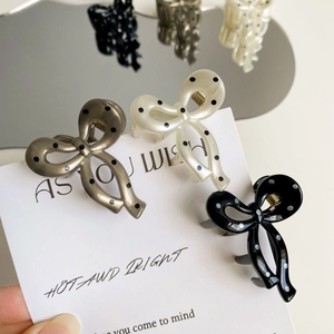 Detailed view of polka dot bow hair claws in white gold and black on display card