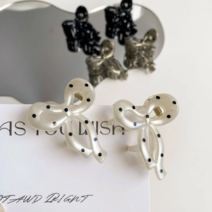 Detailed macro view of cream pearl resin bow hair clips with black polka dots and gold spring