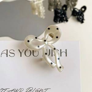 Detail of cream white polka dot bow hair claw clip with glossy pearlescent finish