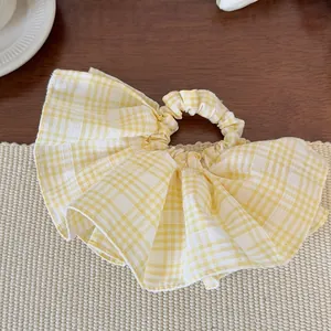 Detail view of yellow plaid scrunchie with layered ruffle design on woven mat