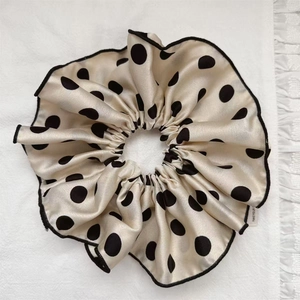 Detailed close-up of champagne polka dot satin scrunchie with elegant black ruffled edges