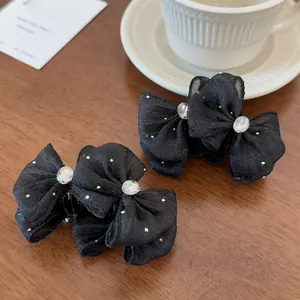 Macro shot of two black tulle bow hair clips with rhinestones on a rustic wooden desk