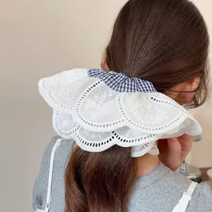 Large white lace embroidery scrunchie with blue checkered detail shown on a ponytail