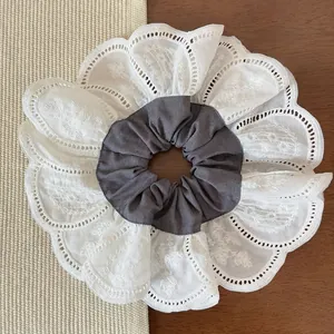 Macro detail of oversized white lace floral embroidery on dark grey elastic scrunchie