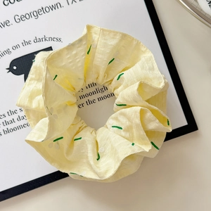 Close-up of fluffy pale yellow floral scrunchie with green leaf pattern on art card