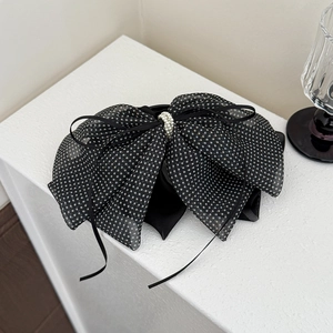 Detailed close-up of a black polka dot mesh bow hair clip with elegant pearl embellishments