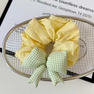 Close-up of yellow scrunchie with green gingham bow on a stylish metal tray