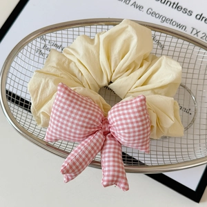Close-up of cream-colored scrunchie with red plaid bow in a silver mesh basket