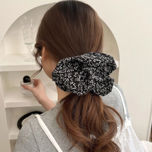 Chouchou élégant en tissu floral noir avec motifs de fleurs blanches porté en queue de cheval