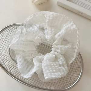 Détail d'un chouchou en seersucker blanc à texture quadrillée dans un panier argenté